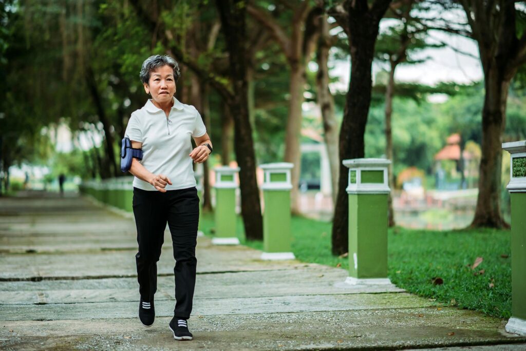 Asian chinese smiling active senior woman running in a park